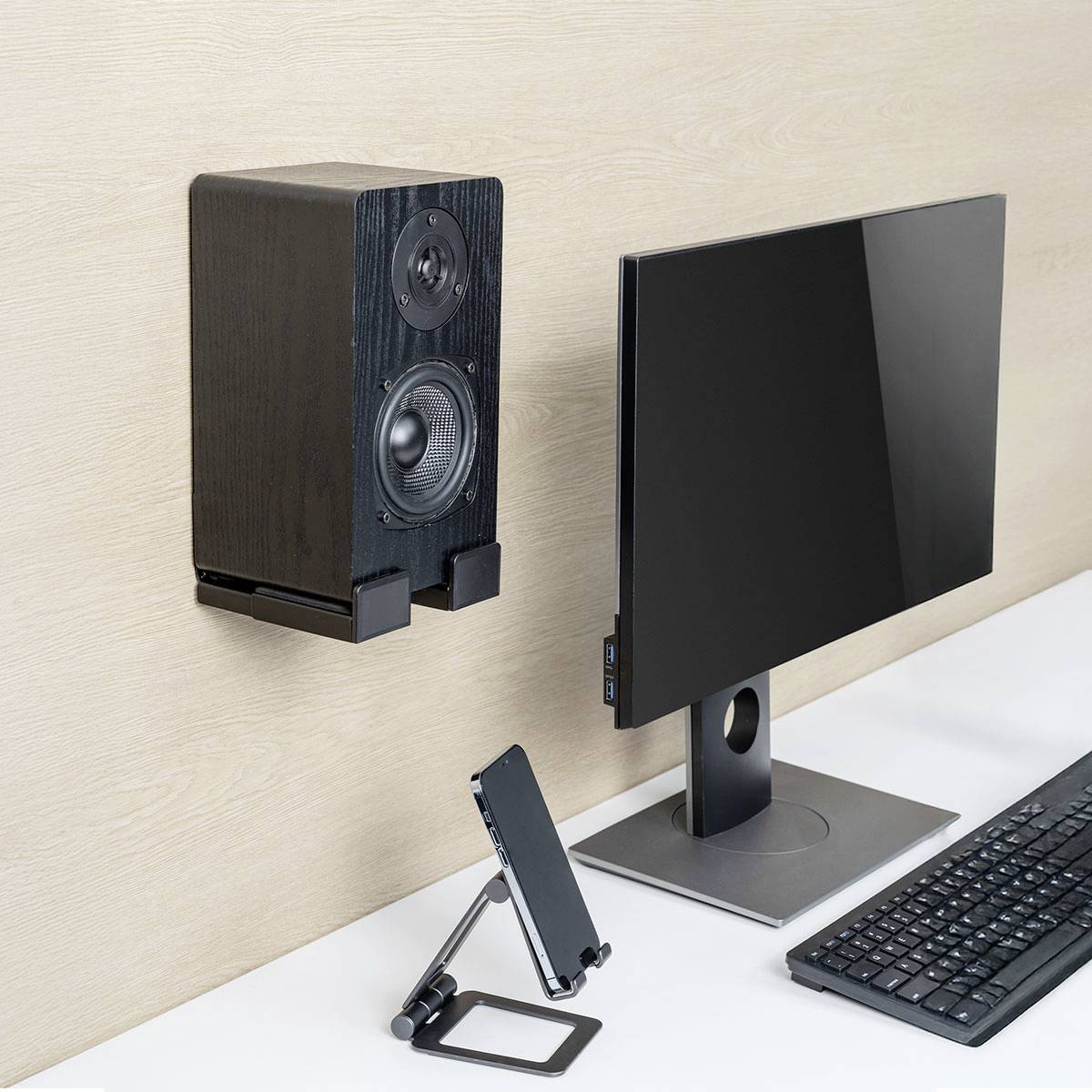 Ein Desktop-Setup mit einem Computermonitor und einem Tablet auf Ständern neben einem an der Wand montierten Lautsprecher. Minimalistisches Design mit neutralen Farben.