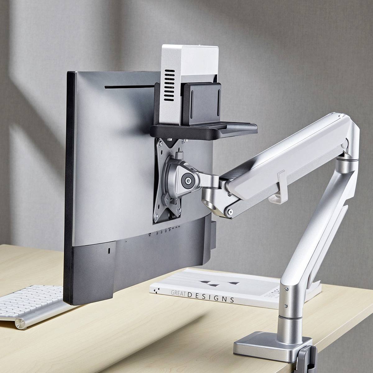 Ein Monitor, der an einem verstellbaren Arm befestigt ist, mit einem kleinen Desktop-Computer, der an der Rückseite angebracht ist. Der Aufbau steht auf einem Holzschreibtisch.