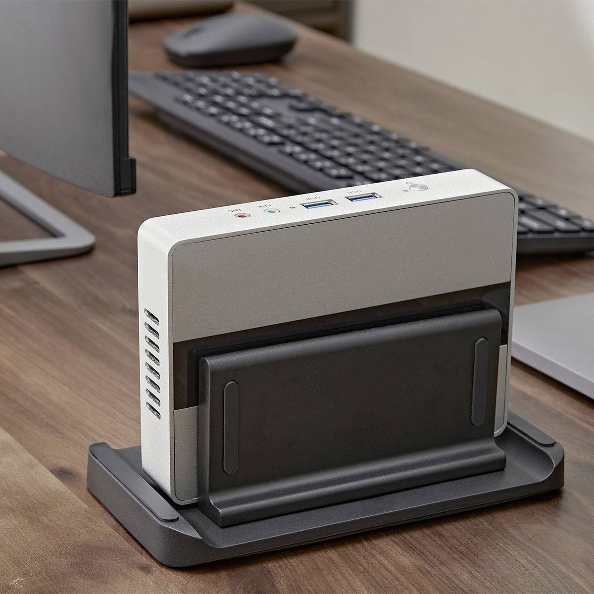 Eine silberne Dockingstation auf einem Schreibtisch, verbunden mit einem Computermonitor und einer Tastatur. Sie verfügt über verschiedene Anschlüsse für Konnektivität.