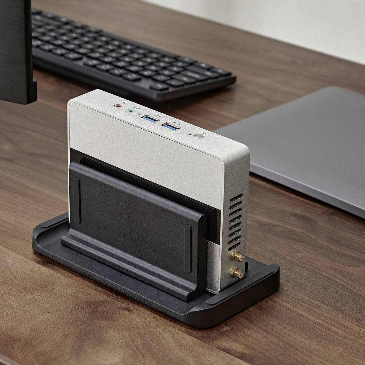 Ein Dockingstation mit einem vertikalen Schlitz und mehreren Anschlüssen steht auf einem Holzschreibtisch, umgeben von einer Tastatur und einem Laptop.