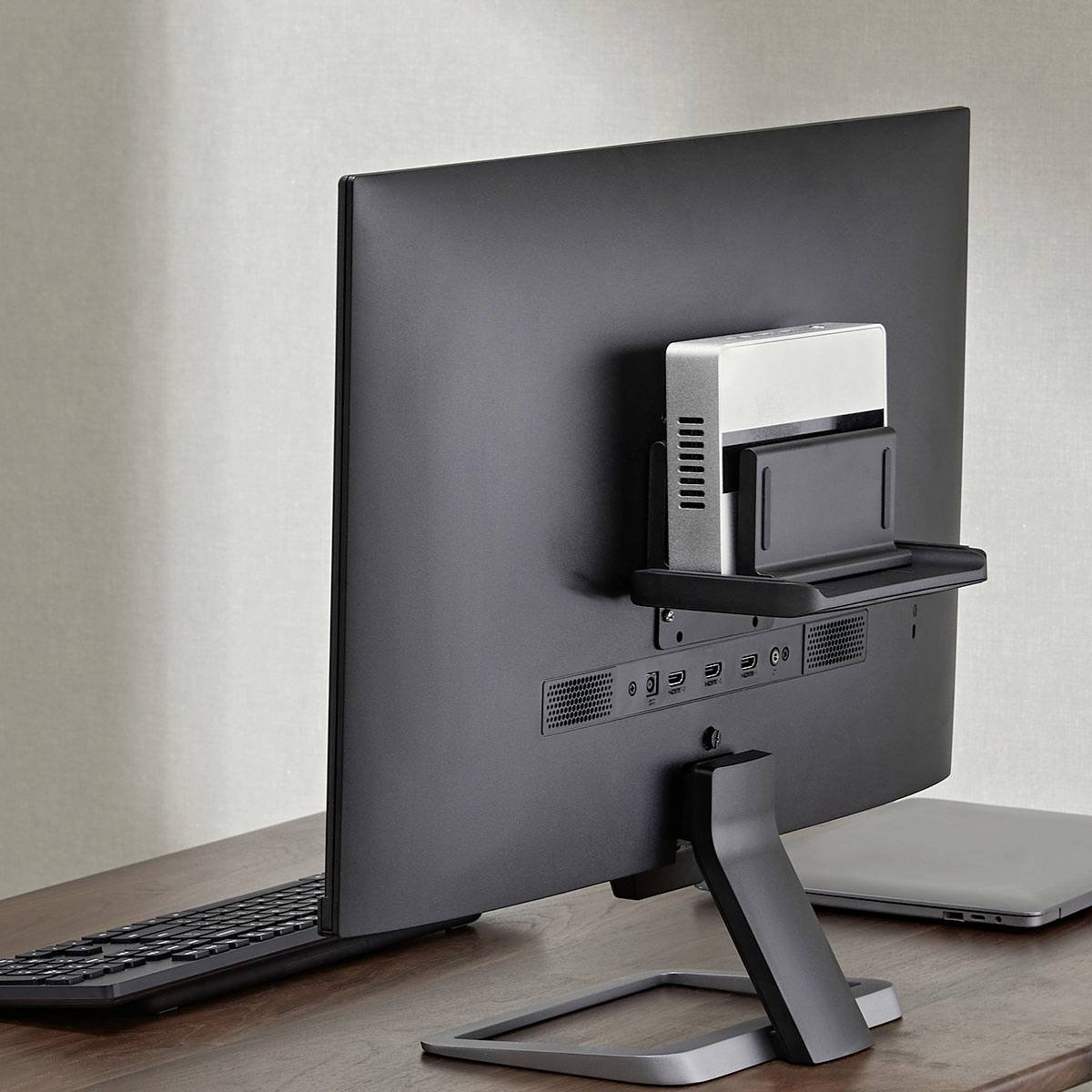 Ein Computermonitor mit einem kleinen rechteckigen Gerät, das auf der Rückseite montiert ist, positioniert auf einem Holzschreibtisch neben einer Tastatur.