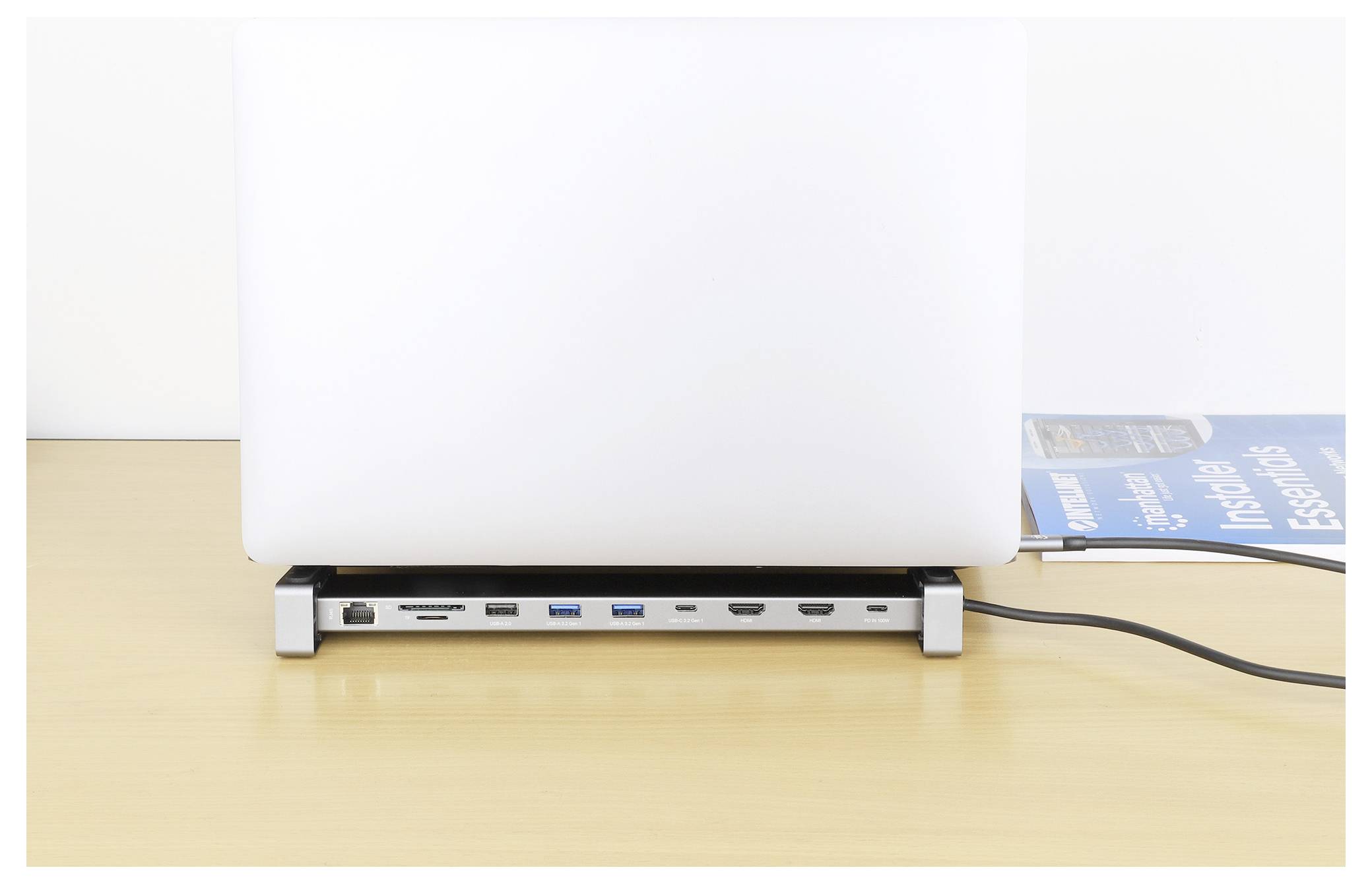 Ein Laptop steht auf einer Docking-Station mit mehreren sichtbaren Anschlüssen, darunter USB, HDMI und Ethernet, auf einem Holzschreibtisch.