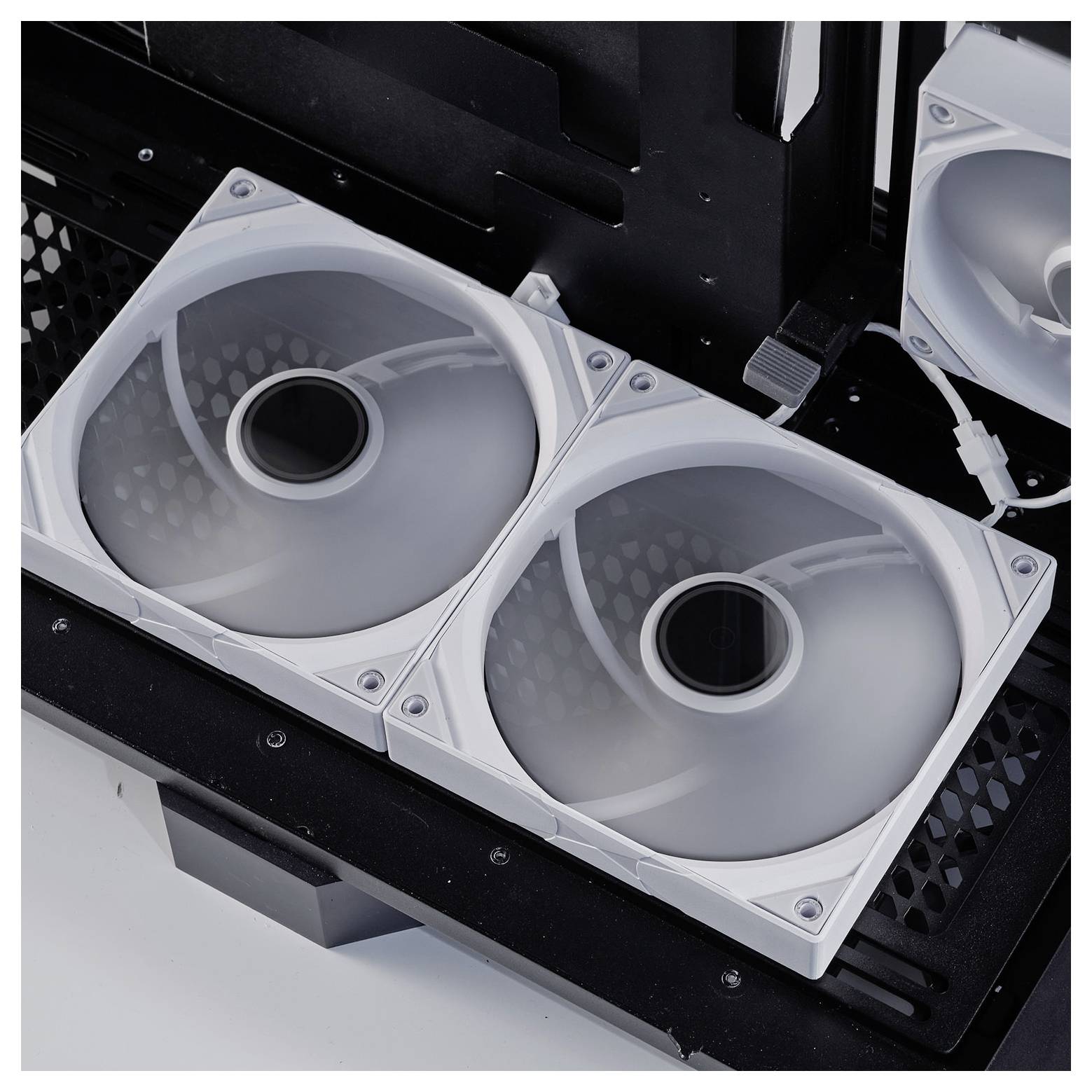 Zwei weiße Kühlventilatoren, die in einem Computergehäuse nebeneinander installiert sind, wobei ein dritter Ventilator im Hintergrund teilweise sichtbar ist.