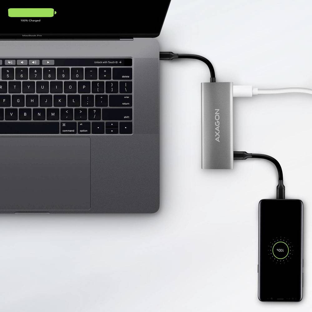 Ein Laptop und ein Smartphone laden über einen USB-Hub. Der Laptop-Bildschirm zeigt '100% geladen', während das Telefon ein Ladensymbol anzeigt.