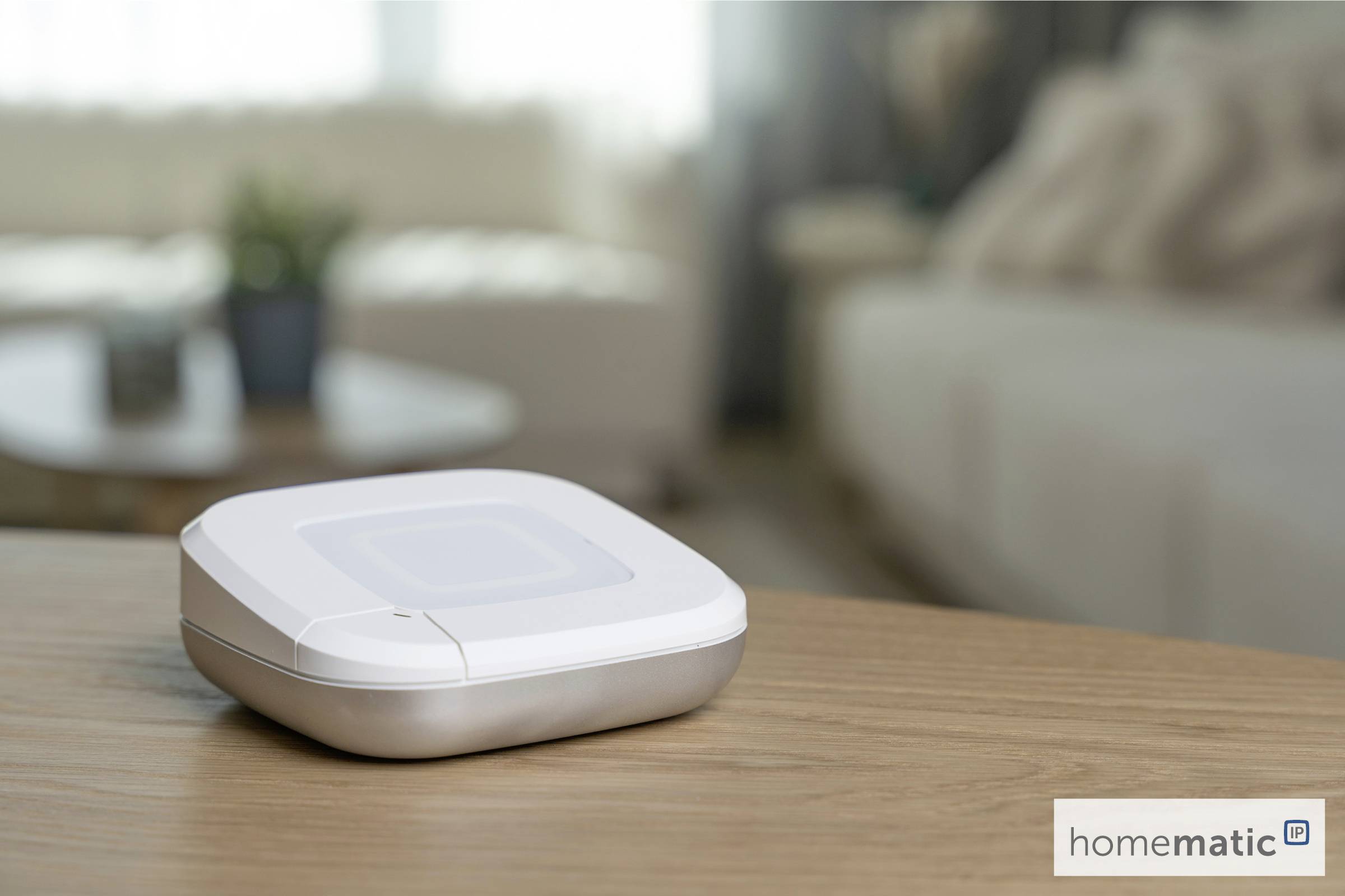 Ein Smart-Home-Gerät steht auf einem Holztisch in einem Wohnzimmer. Der Hintergrund zeigt verschwommene Sofas und eine Pflanze und schafft eine gemütliche Atmosphäre.