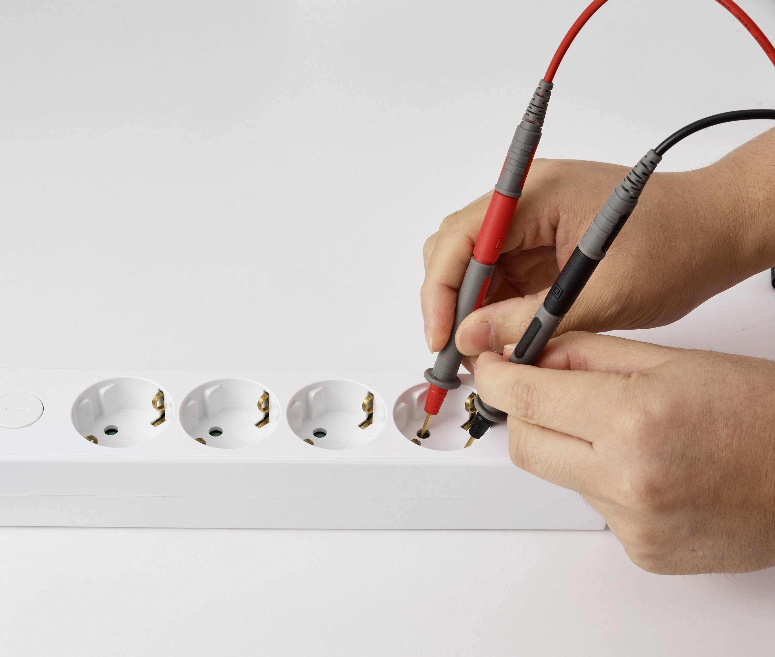 Eine Person verwendet ein Multimeter, um die Spannung einer Steckdosenleiste zu überprüfen und damit eine elektrische Sicherheitskontrolle durchzuführen.