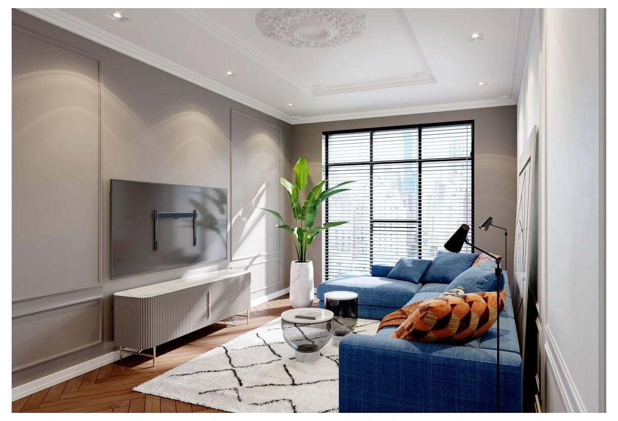 Ein modernes Wohnzimmer mit einem blauen Ecksofa, bunten Kissen, einem an der Wand montierten Fernseher, einer großen Pflanze und einem Fenster mit Jalousien.