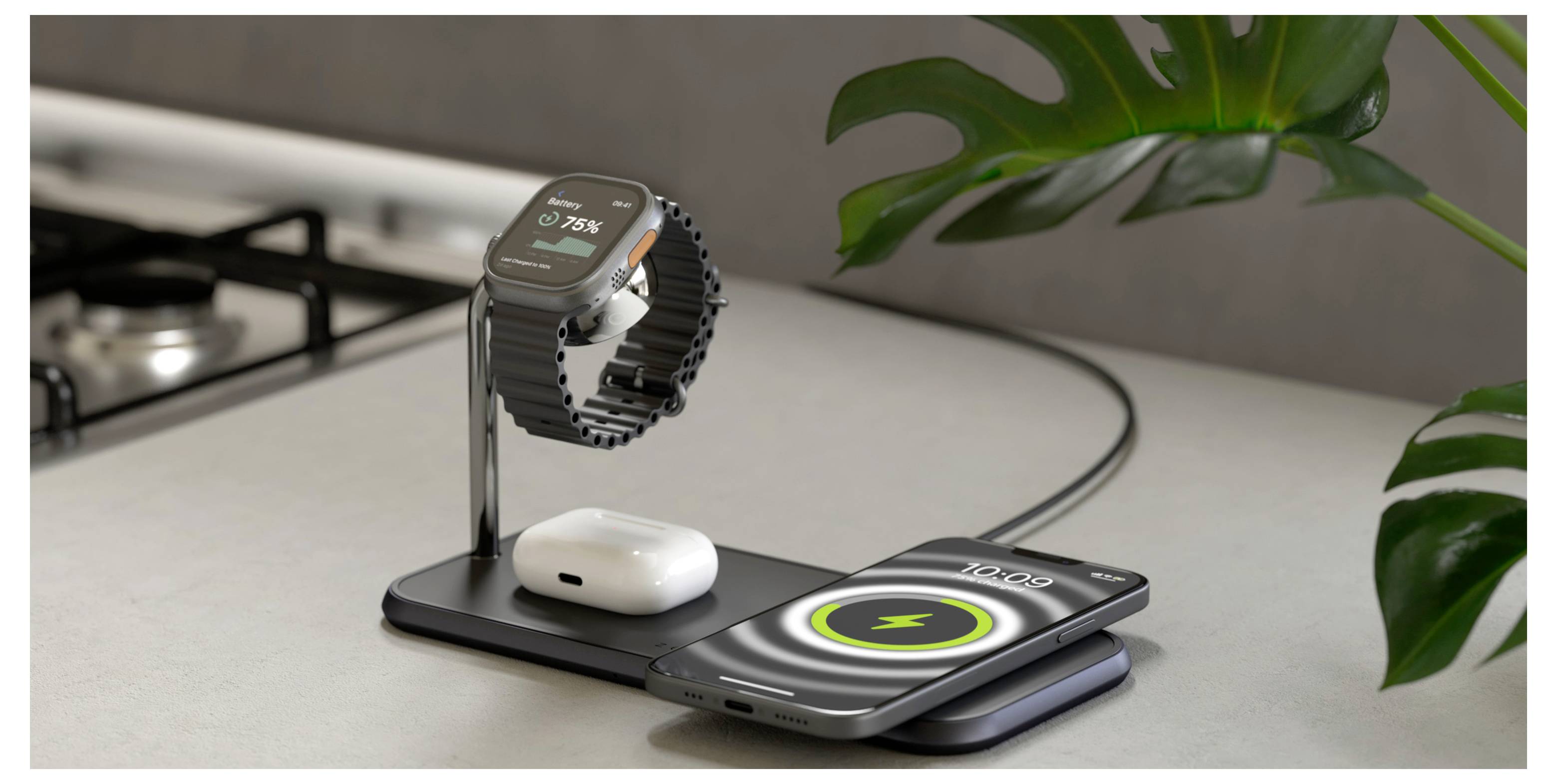 Eine Smartwatch, kabellose Kopfhörer und ein Smartphone laden auf einer eleganten, modernen Ladestation auf einer Küchenarbeitsplatte neben einer grünen Pflanze.
