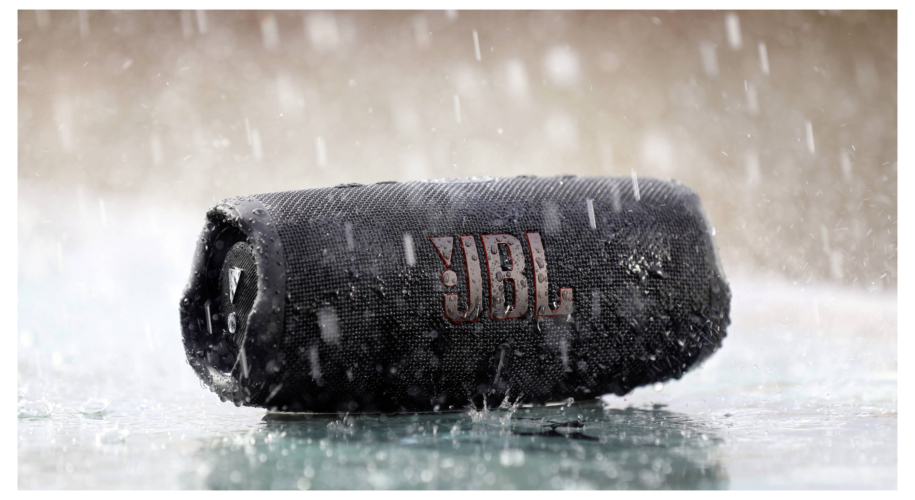 Ein schwarzer JBL-Portablelautsprecher widersteht heftigem Regen auf einer nassen Oberfläche und zeigt damit seine wasserdichte Eigenschaft.