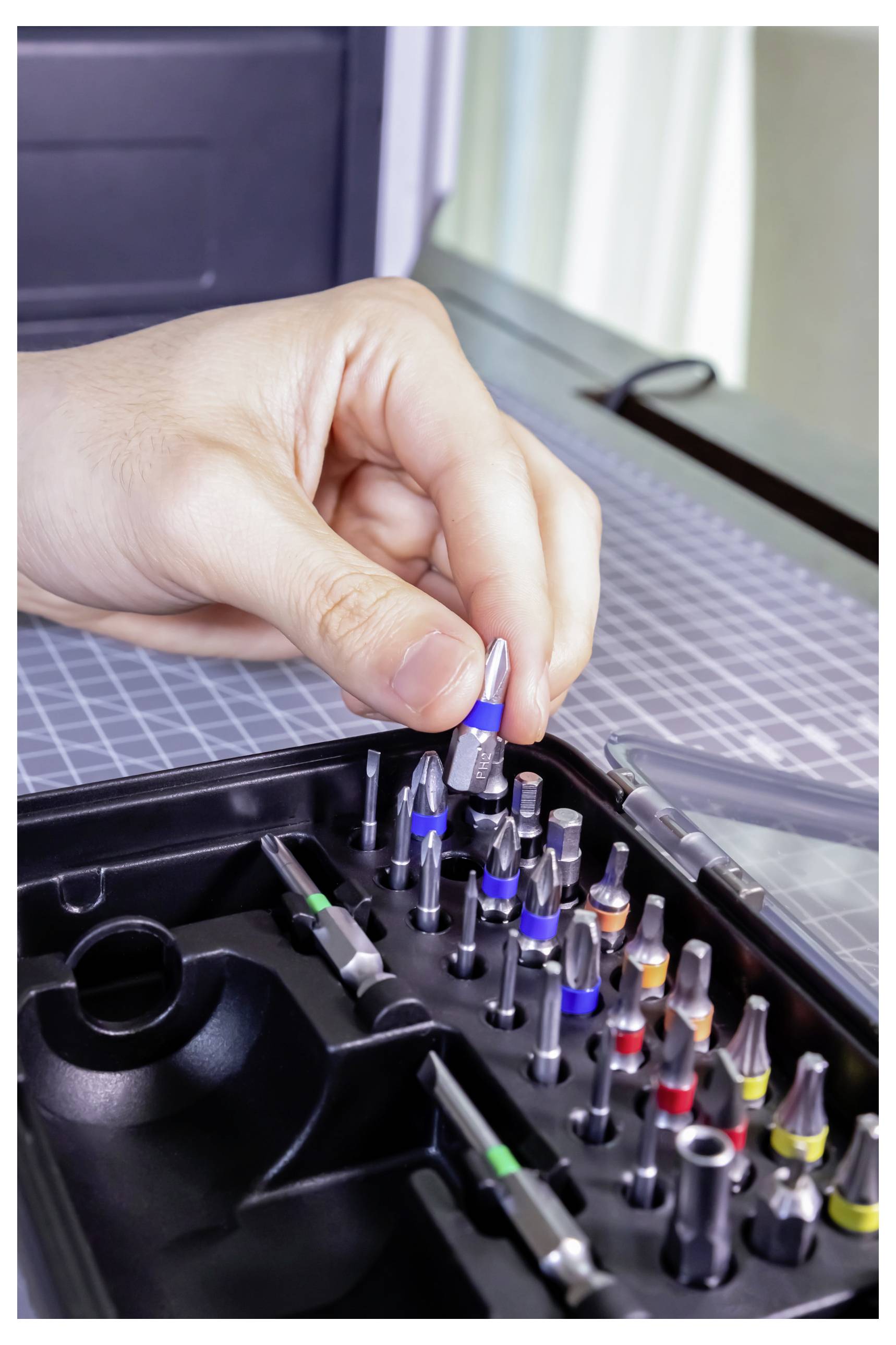 Eine Hand, die einen blaugriffigen Bohrer aus einem Satz mit verschiedenfarbigen Bohrern auswählt, was einen Fokus auf präzise Werkzeugauswahl andeutet.