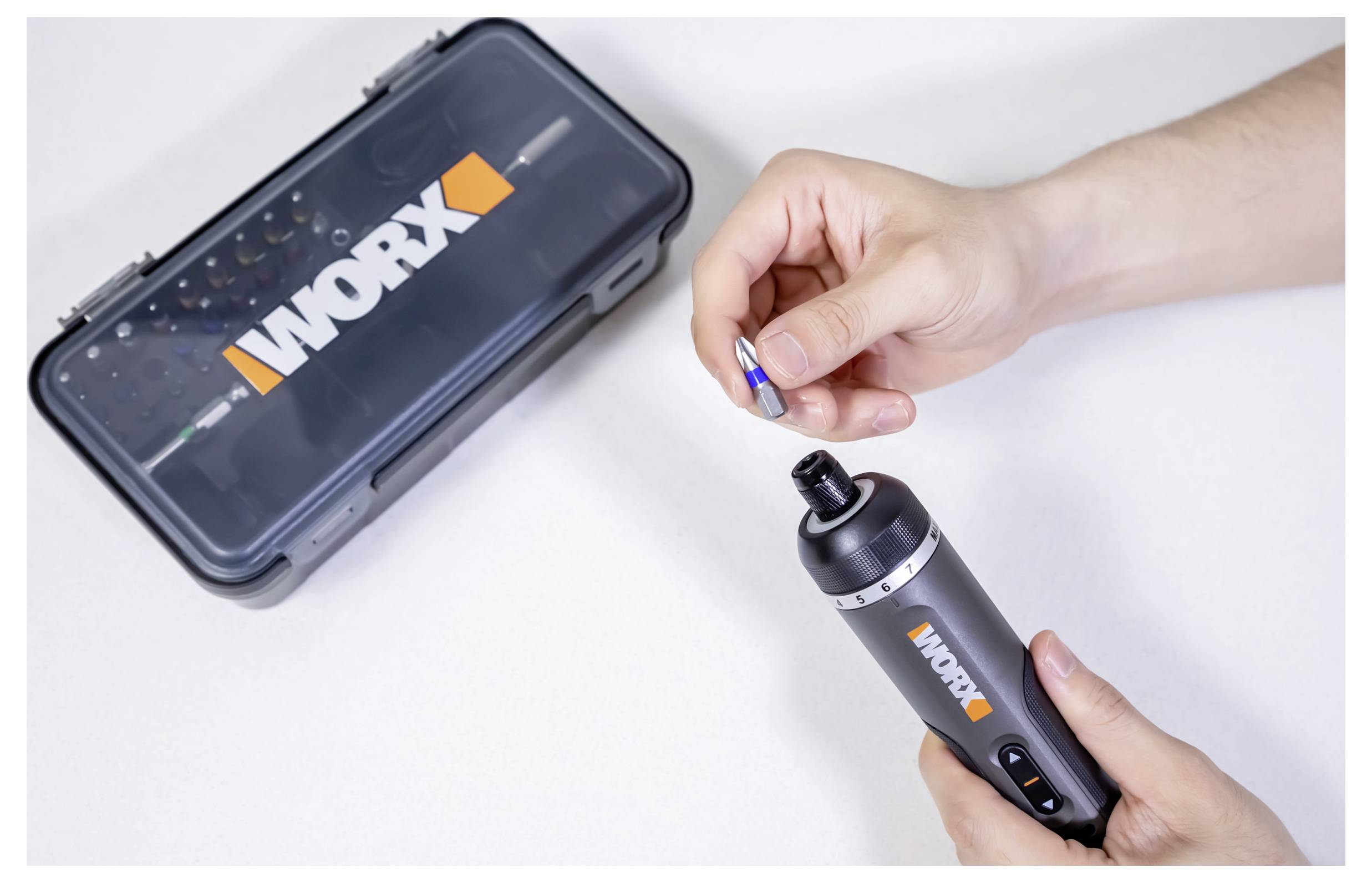 Eine Person steckt einen Bohrer in einen grauen kabellosen Akkuschrauber neben einer Werkzeugkiste mit der Aufschrift „Worx