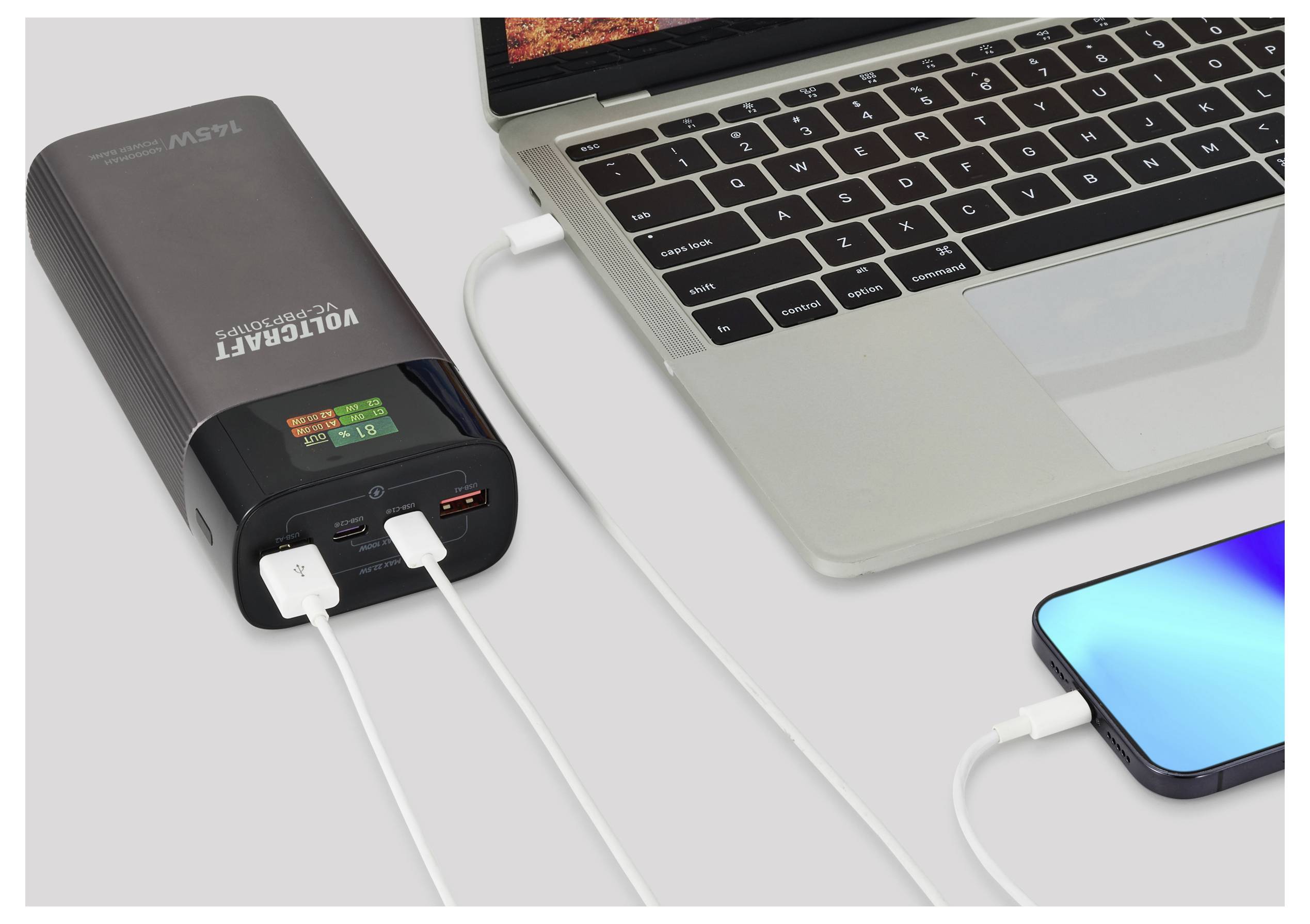 Ein Powerbank, die einen Laptop und ein Smartphone gleichzeitig lädt. Der Laptop ist in Gebrauch mit geöffnetem Bildschirm, und das Handy zeigt einen blauen Bildschirm.