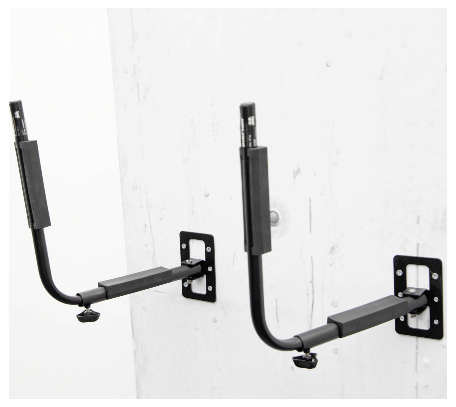 Zwei schwarze an der Wand montierte Fahrradständer an einer weißen Wand, jeder mit einem gepolsterten horizontalen Arm und einer gekrümmten Stützklammer.