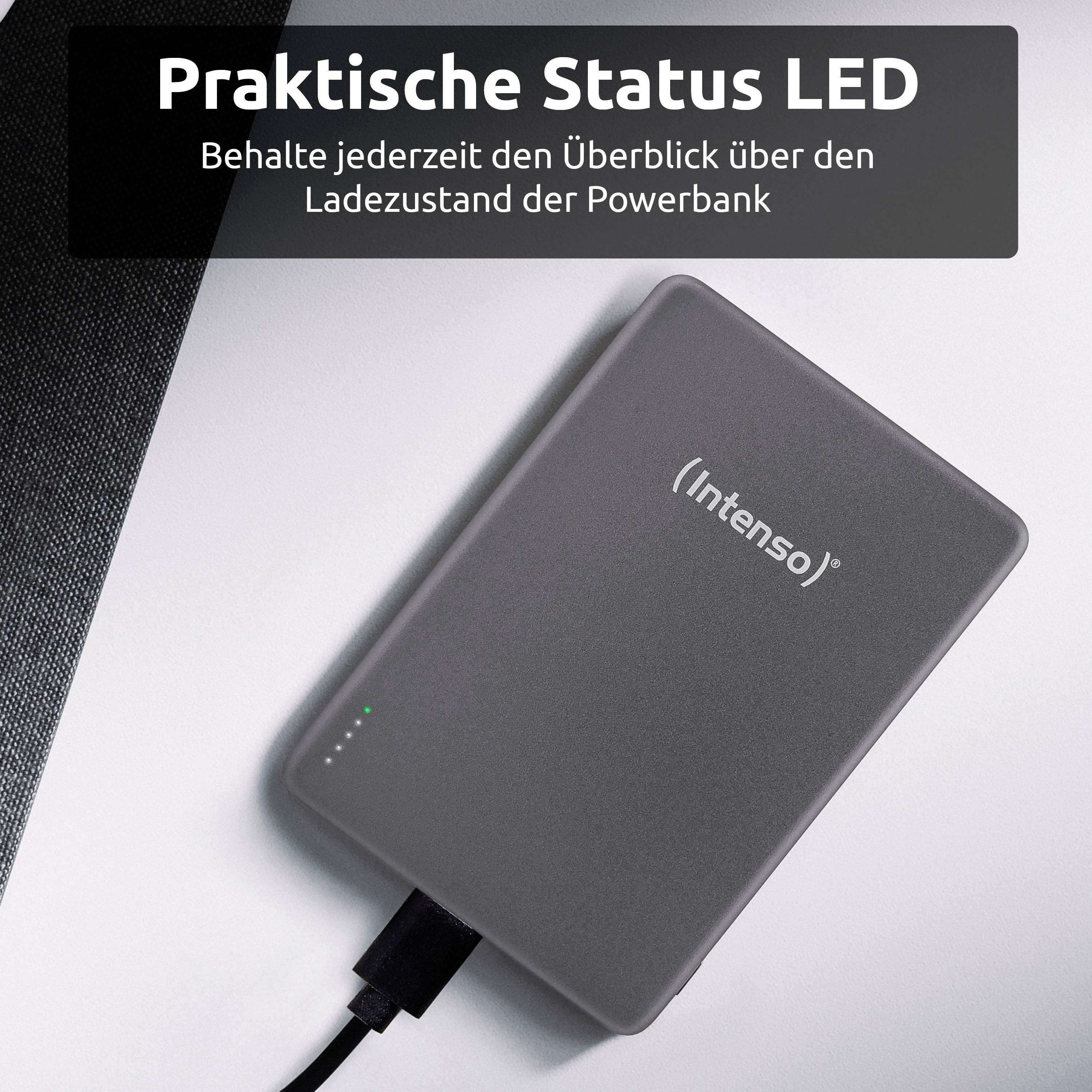 Ein grauer Intenso Powerbank mit einer Status-LED-Anzeige wird geladen und liegt auf einer weißen Oberfläche. Ein Text auf Deutsch erwähnt die Überwachung des Ladestatus.