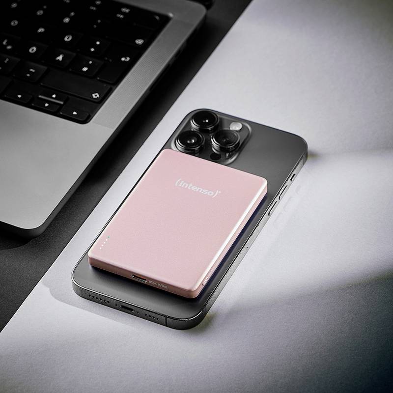 Ein Smartphone, ein pinker Intenso-Powerbank und ein teilweise sichtbarer Laptop auf einem Schreibtisch, was eine technische oder Arbeitsumgebung andeutet.