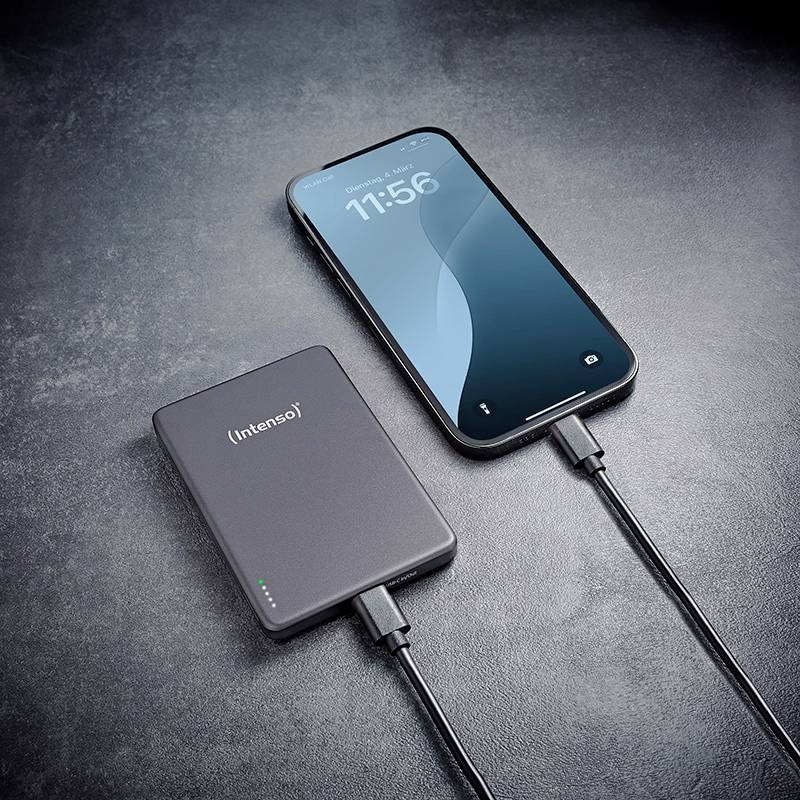 Ein Smartphone ist über ein Kabel mit einer externen Powerbank auf einer dunklen Oberfläche verbunden und zeigt einen Ladevorgang.