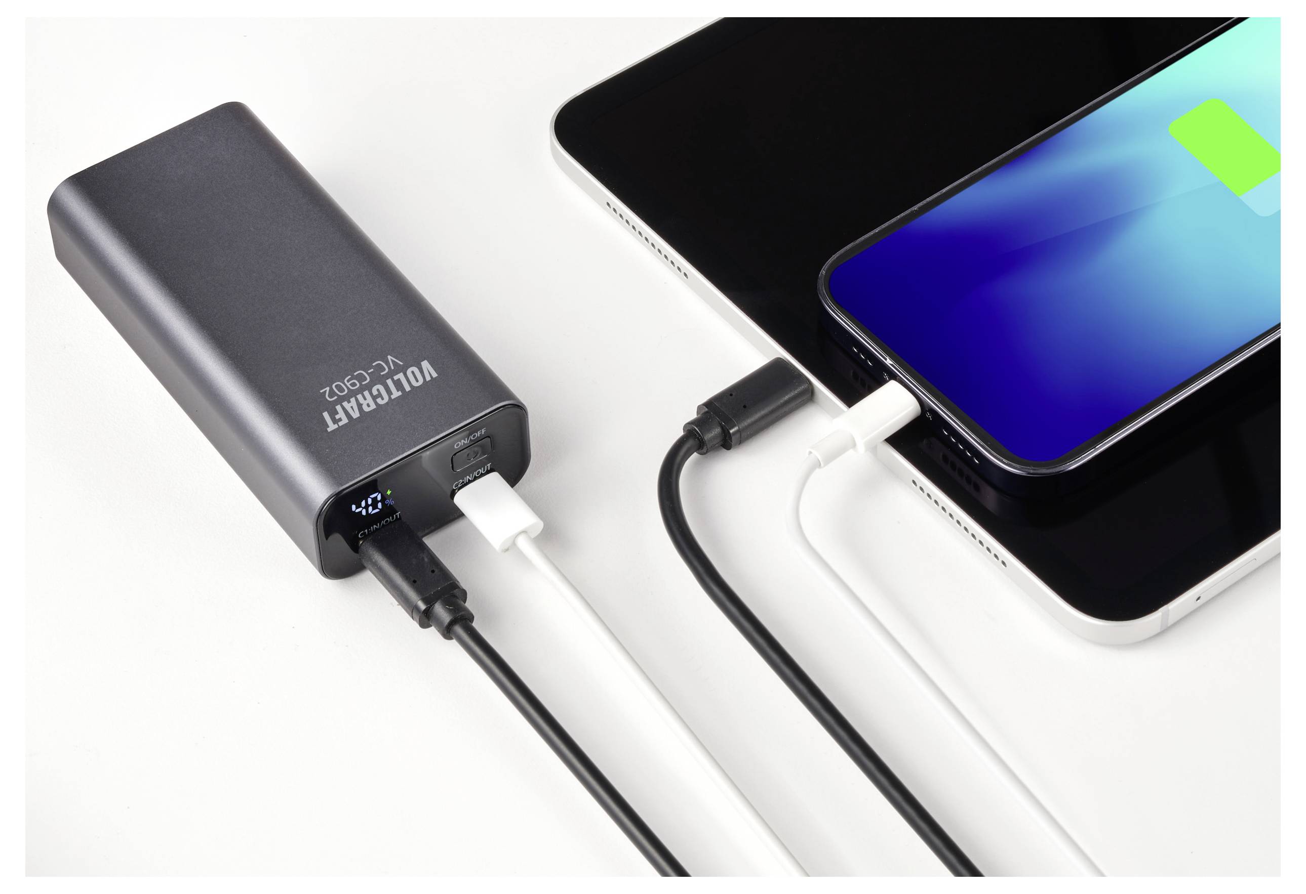 Eine Powerbank lädt gleichzeitig ein Smartphone und ein Tablet. Der Bildschirm des Telefons zeigt ein Ladesymbol.