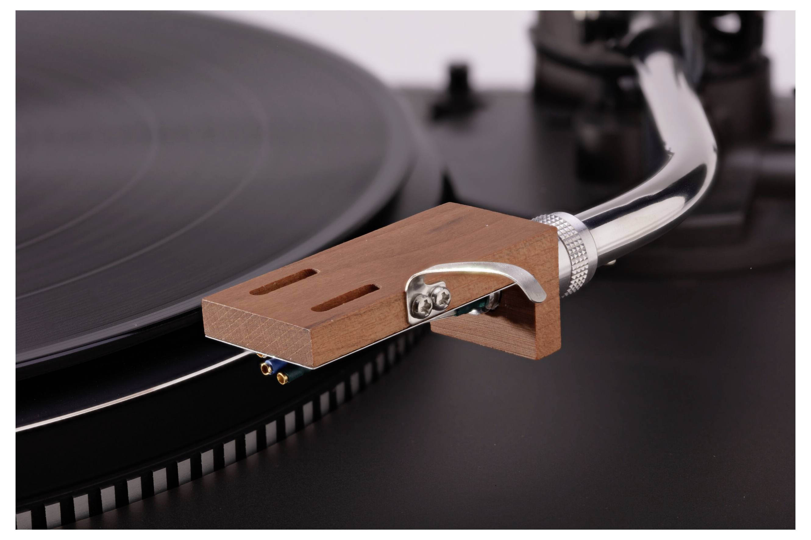 Nahaufnahme des Tonarms und der Nadel eines Plattenspielers auf einer Vinylplatte, die den Holztonabnehmer und die präzise Ingenieurskunst des Geräts zur Schau stellt.