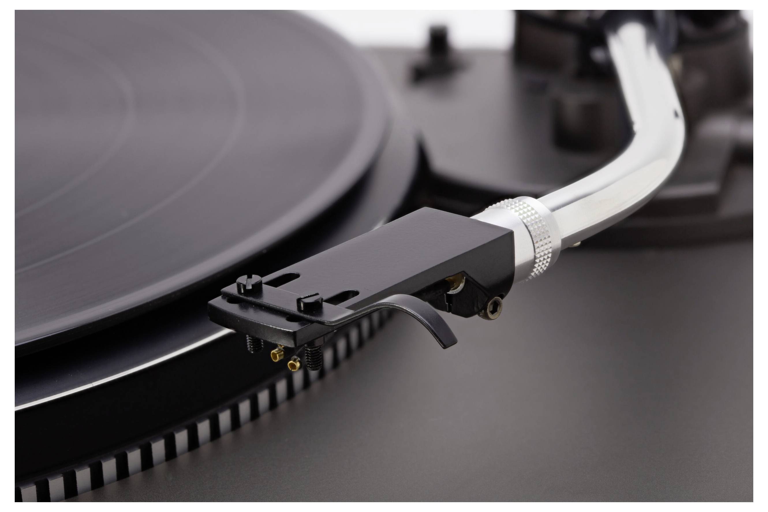 Nahaufnahme eines Plattenspielers mit Fokus auf die Nadel und den Tonarm, der über einer schwarzen Vinylplatte positioniert ist.