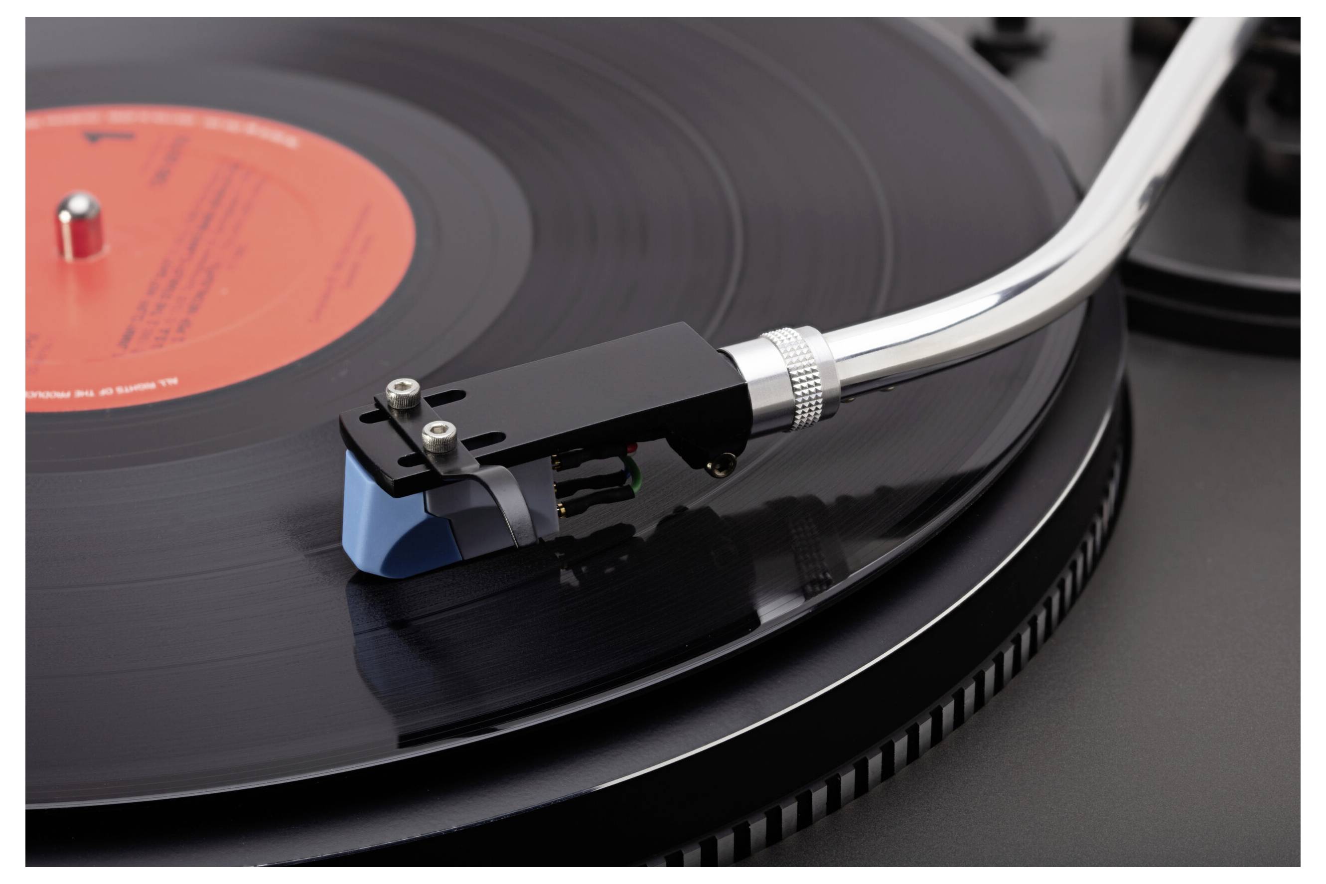 Eine Nahaufnahme eines Plattenspielers, der eine schwarze Schallplatte abspielt; der Fokus liegt auf dem Tonarmen, der auf der sich drehenden Platte positioniert ist.