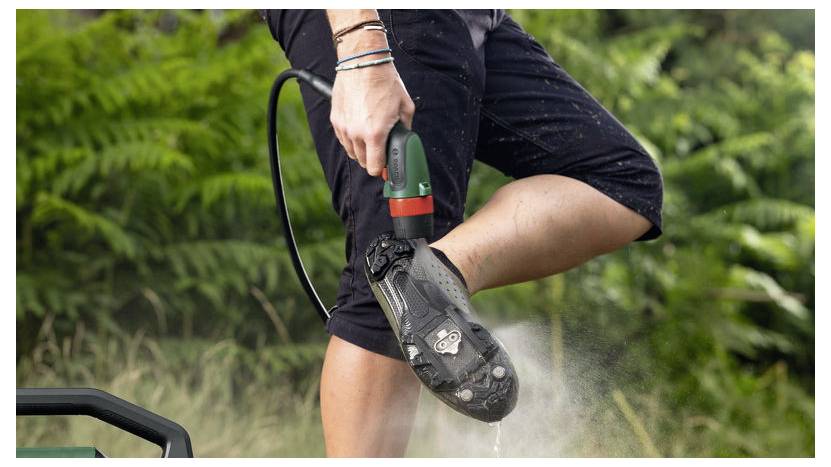 Eine Person reinigt ihren Schuh mit einem Hochdruckreiniger in einer Gartenumgebung und betont dabei die Reinigungseffizienz und Outdoor-Aktivität.