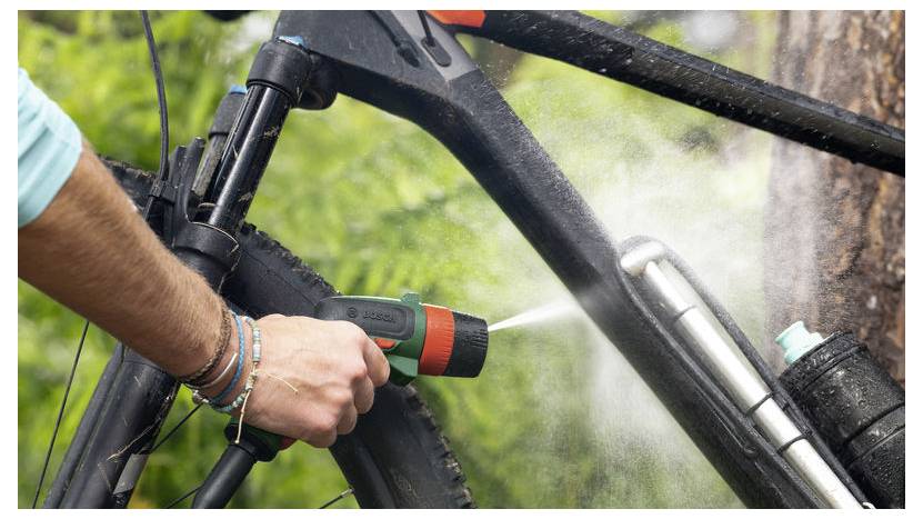 Eine Person verwendet einen Schlauchadapter, um Wasser zu spritzen und einen schwarzen Fahrradrahmen in der Nähe einer Waldlandschaft zu reinigen.