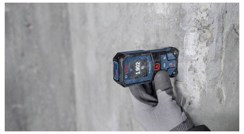 Eine Person mit einem Handschuh verwendet einen digitalen Entfernungsmesser an einer Betonwand. Das Gerät zeigt '1,902' an.