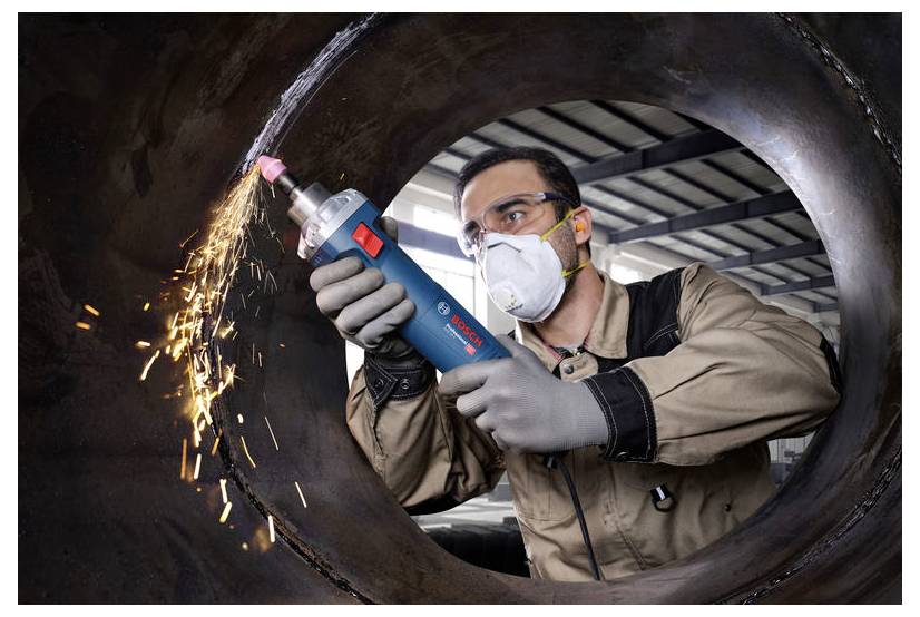 Eine Person in Schutzausrüstung nutzt ein blaues, tragbares Elektrowerkzeug zum Schleifen von Metall, wobei Funken in einer industriellen Umgebung sprühen.