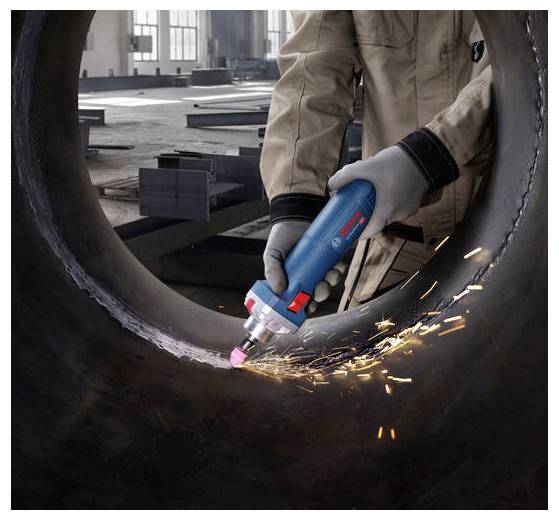 Eine Person in einer Werkstatt verwendet ein blau-rotes tragbares Elektrowerkzeug, um das Innere eines großen Metallrohrs zu schleifen und dabei Funken zu erzeugen.