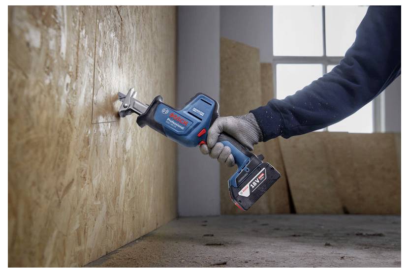Eine Person verwendet eine blaue elektrische Säge, um ein Holzbrett in einem teilweise fertiggestellten Raum zu schneiden. Licht fällt durch ein nahegelegenes Fenster ein.