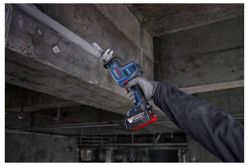 Eine Person verwendet eine blaue kabellose Säbelsäge, um in einem industriellen Umfeld ein Metallrohr zu durchtrennen und trägt dabei Schutzhandschuhe.