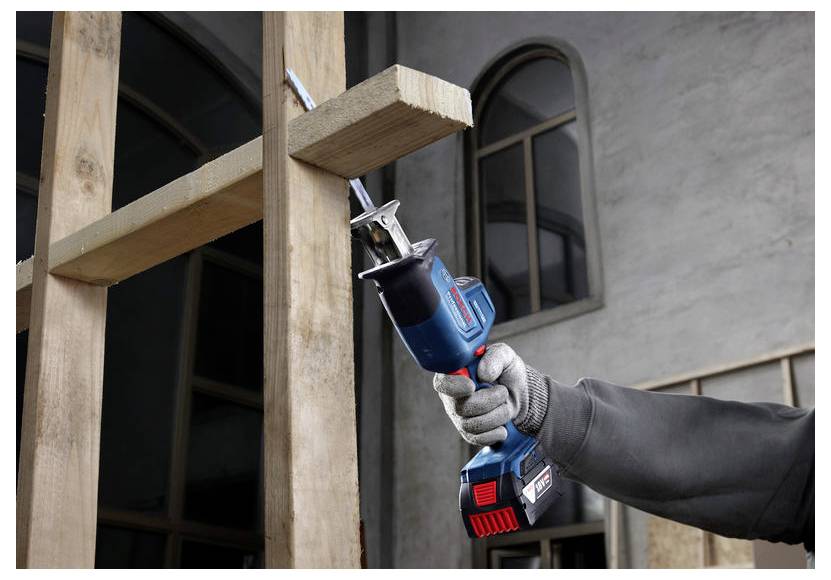 Eine Person verwendet eine kabellose Säbelsäge mit blau-rotem Design, um einen Holzbalken in Innenräumen zu zersägen.