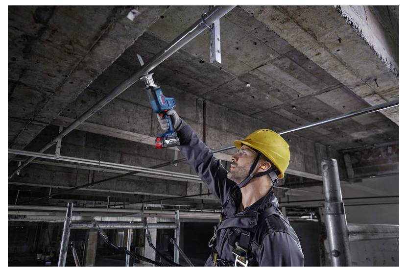 Arbeiter mit gelbem Schutzhelm, der ein Elektrowerkzeug verwendet, um Metallrohre an einer Betondecke zu installieren und damit Bauarbeiten durchführt.