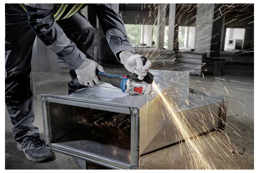 Eine Person mit Sicherheitsausrüstung verwendet ein Elektrowerkzeug, um Metallkanäle zu schneiden, wobei Funken in einem Industriegebäude entstehen.