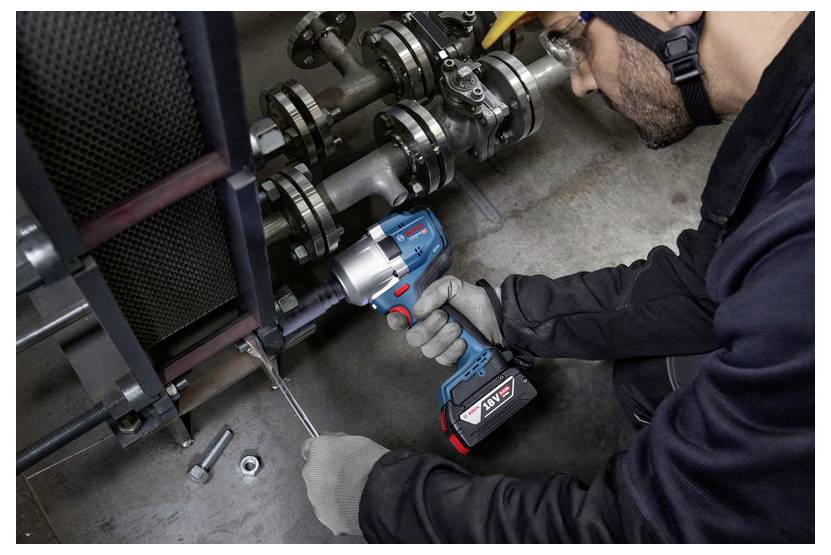 Eine Person mit Schutzausrüstung verwendet ein Elektrowerkzeug, um Bolzen an industrieller Maschinerie zu befestigen.