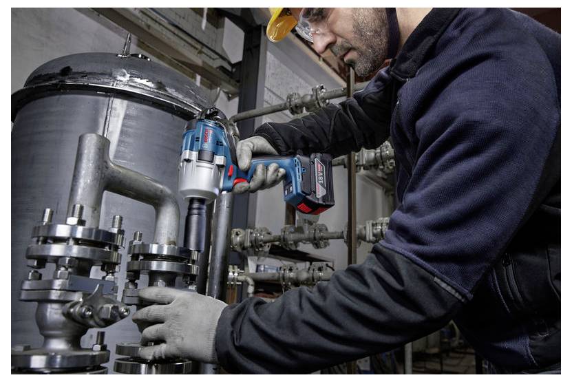 Eine Person mit Sicherheitsausrüstung verwendet ein kabelloses Elektrowerkzeug, um Wartungsarbeiten an industriellen Rohrleitungen durchzuführen und damit Arbeiten in einem industriellen Umfeld anzuzeigen.