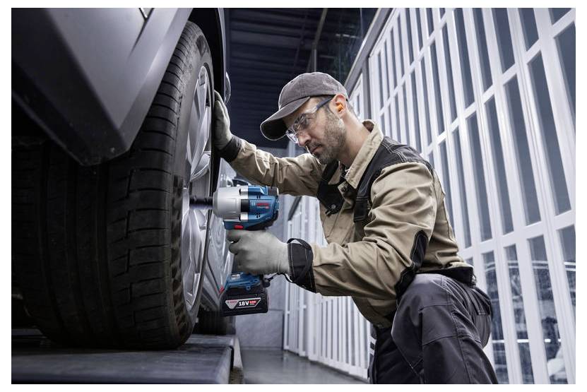 Ein Mechaniker in Schutzausrüstung verwendet ein Elektrowerkzeug, um ein Autorad in einer Garage zu befestigen und dabei Fahrzeugwartung und Sicherheit zu betonen.