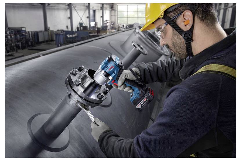 Ein Arbeiter in Sicherheitsausrüstung verwendet ein Elektrowerkzeug, um einen Bolzen an einer großen industriellen Rohrleitung in einer Fabrikhalle zu befestigen.