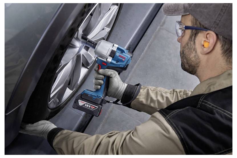 Eine Person benutzt einen kabelosen Schlagschrauber, um ein Autorad zu befestigen. Das Werkzeug zeigt '18 V' an, und der Benutzer trägt Sicherheitsausrüstung einschließlich Handschuhen und Schutzbrille.
