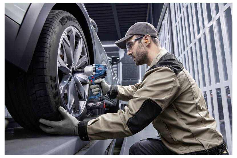 Ein Mechaniker verwendet ein Elektrowerkzeug, um Schrauben an einem Autorad in einer Garage zu befestigen und trägt dabei Schutzhandschuhe und eine Schutzbrille.