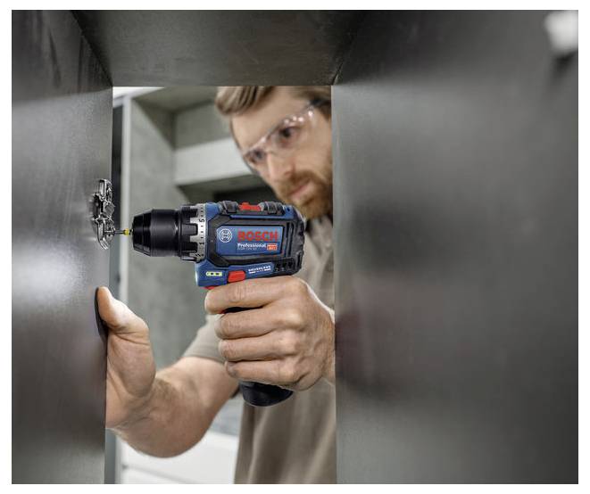 Eine Person mit Sicherheitsbrille verwendet einen Bosch-Akkuschrauber auf einer Metalloberfläche und konzentriert sich auf präzise Bau- oder Reparaturarbeiten im Innenbereich.