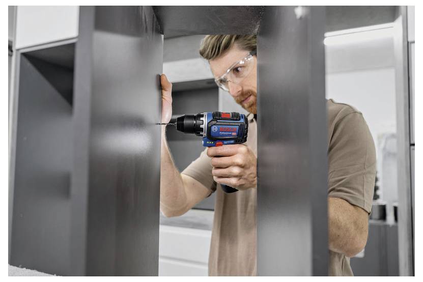 Eine Person in einer Werkstatt, die mit einer Bohrmaschine ein Möbelstück zusammenbaut und dabei Schutzbrille zum Eigenschutz trägt.