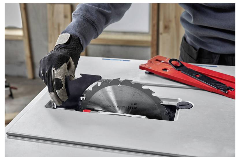 Eine Person mit Handschuhen justiert eine kreisförmige Sägeblatt an einer Tischkreissäge, wobei sich ein roter Winkelführer in der Nähe befindet und einen Holzbearbeitungsaufbau andeutet.