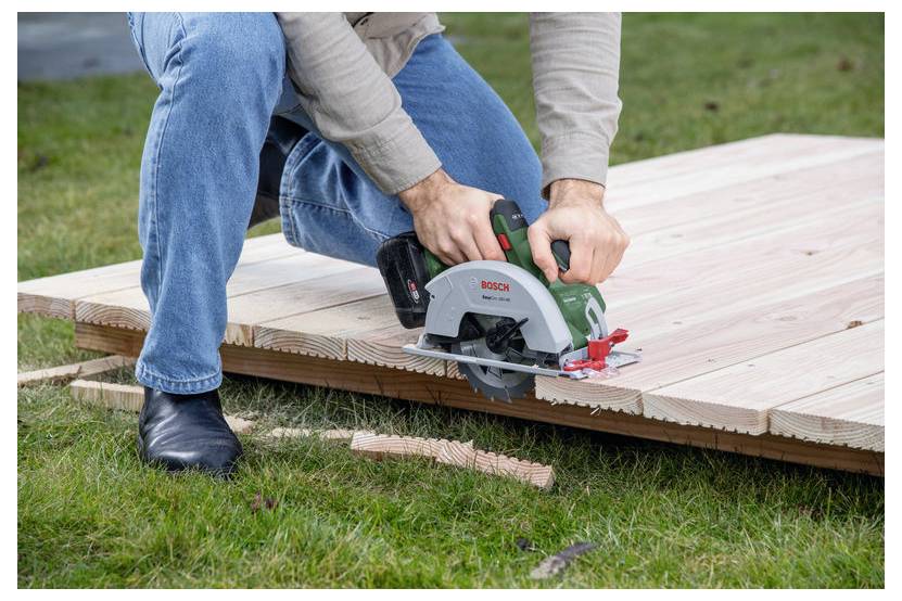 Eine Person verwendet eine Kreissäge, um Holzbretter auf Gras zu schneiden und dabei Holzarbeiten oder Bauarbeiten zu demonstrieren.