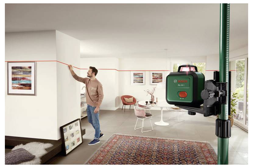 Eine Person, die ein Lasernivelliergerät verwendet, um eine gerade Linie an einer weißen Wand in einem modernen Wohnzimmer zu ziehen, was Heimwerkerarbeiten andeutet.