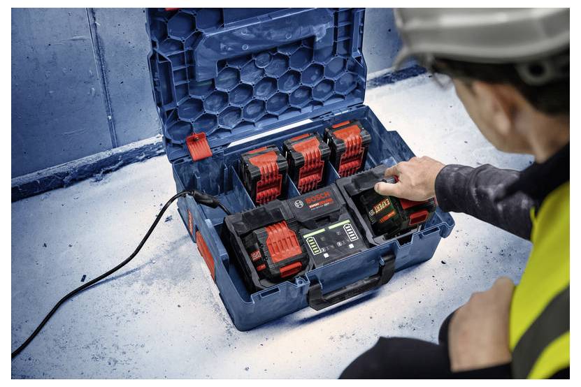 Eine Person in Arbeitskleidung nutzt eine Bosch-Batterieladestationen mit mehreren Batterien in einem blauen Koffer.