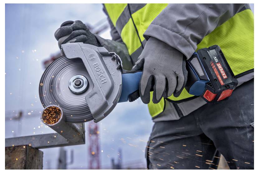 Ein Bauarbeiter verwendet eine Winkelschleifer, um Metall zu schneiden und dabei Funken zu erzeugen. Der Arbeiter trägt eine Warnweste und Handschuhe.