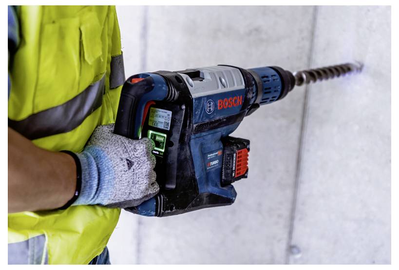 Eine Person mit einer gelben Sicherheitsweste und Handschuhen bohrt mit einem Bosch-Akkuschrauber in eine Betonwand.