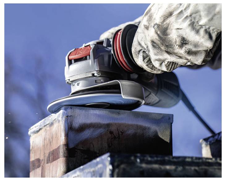Person, die einen Winkelschleifer auf einer Metalloberfläche im Freien verwendet, trägt Schutzkleidung; Funken sind sichtbar, Himmel im Hintergrund.