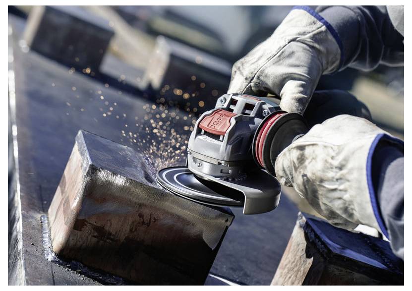 Eine Person mit Schutzhandschuhen schleift eine Metalloberfläche mit einem Elektrowerkzeug; Funken sprühen und deuten auf aktive Metallbearbeitung hin.